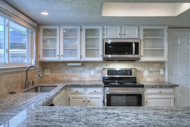 kitchen with a sink, light stone countertops, appliances with stainless steel finishes, and white cabinetry