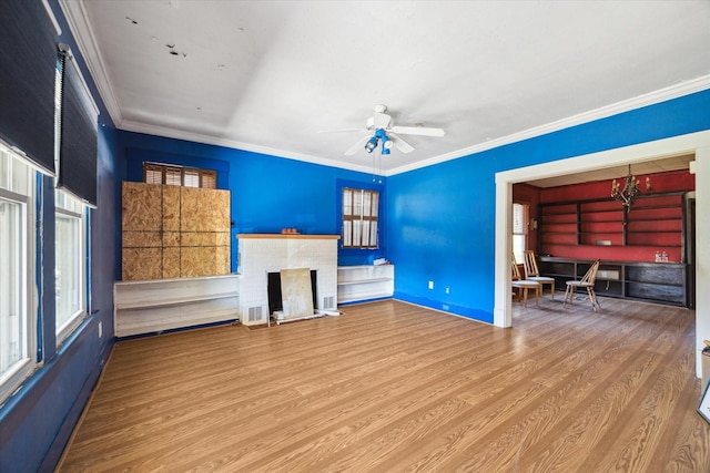 unfurnished living room with a ceiling fan, wood finished floors, a fireplace, ornamental molding, and a wealth of natural light