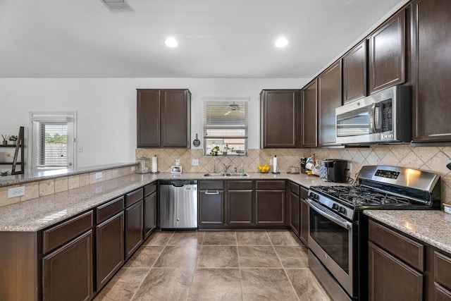 kitchen with backsplash, dark brown cabinets, a peninsula, stainless steel appliances, and a sink