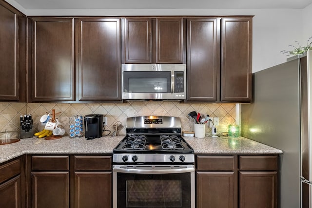 kitchen featuring backsplash, stainless steel appliances, light stone countertops, and dark brown cabinetry