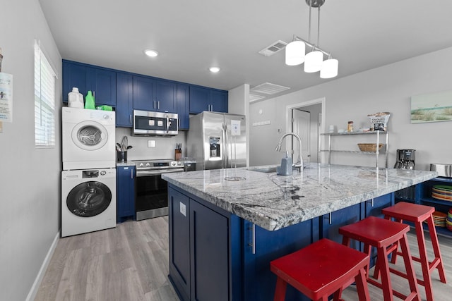 kitchen featuring blue cabinetry, a kitchen breakfast bar, stainless steel appliances, stacked washer / drying machine, and a sink