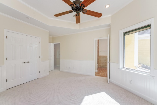 unfurnished bedroom with ornamental molding, carpet flooring, wainscoting, a closet, and a raised ceiling