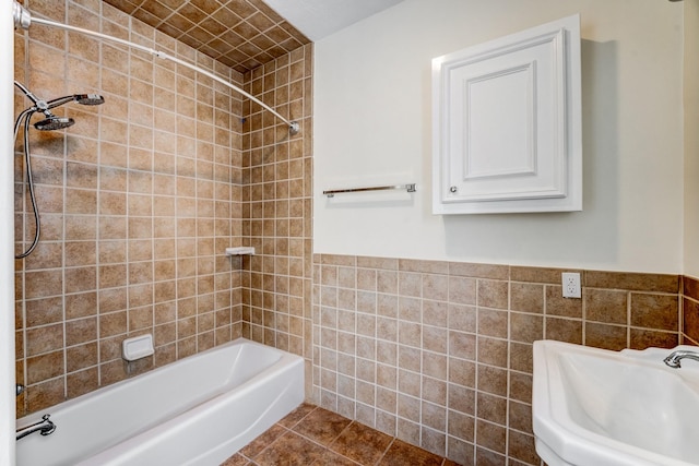 bathroom featuring a wainscoted wall, a sink, tile walls,  shower combination, and tile patterned flooring