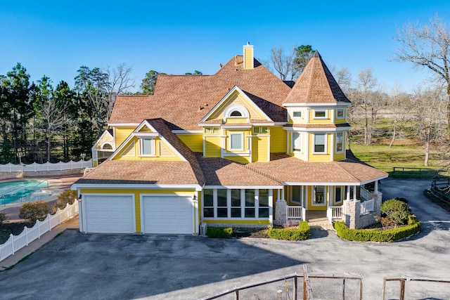 victorian home featuring driveway, a porch, fence, a shingled roof, and a chimney