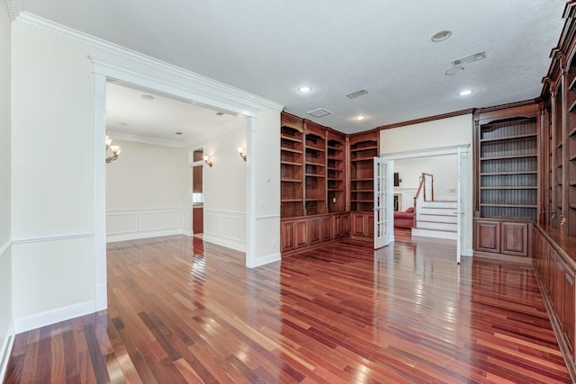 unfurnished room with built in shelves, ornamental molding, wainscoting, wood finished floors, and a decorative wall