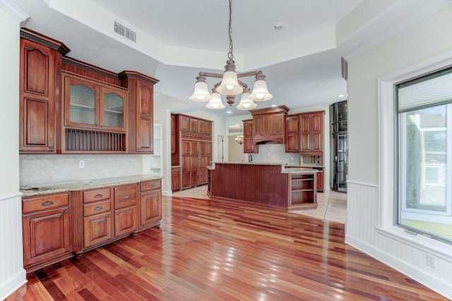 kitchen with a wainscoted wall, light wood-type flooring, open shelves, a tray ceiling, and a chandelier