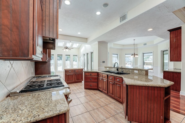 kitchen featuring light stone counters, visible vents, a sink, a raised ceiling, and backsplash