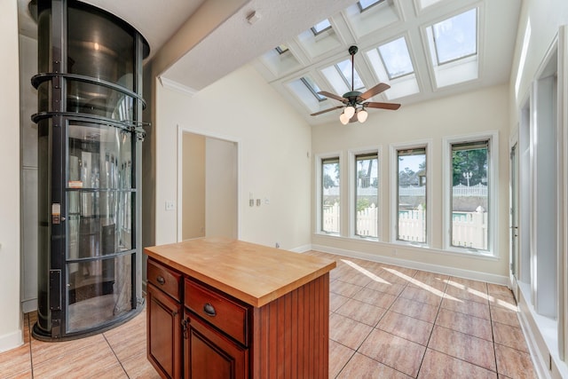 kitchen featuring wood counters, vaulted ceiling with skylight, light tile patterned floors, baseboards, and ceiling fan