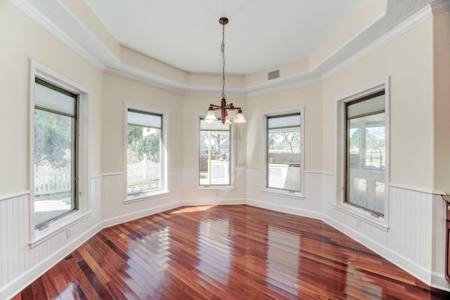 unfurnished dining area featuring a notable chandelier, a wainscoted wall, a raised ceiling, and dark wood-style floors