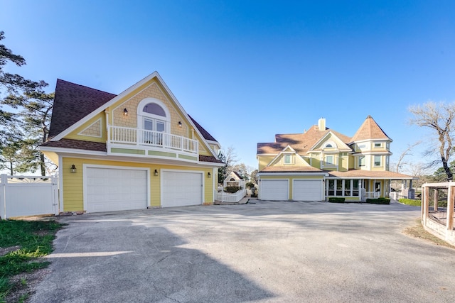 view of front of house featuring a garage, a balcony, concrete driveway, and fence