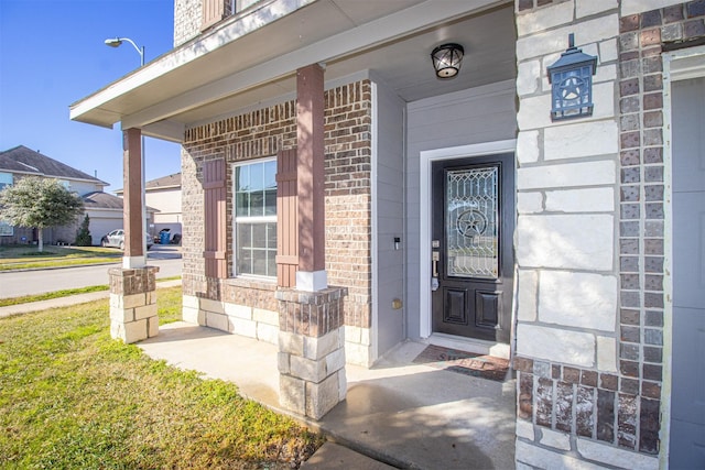 view of exterior entry with brick siding and a porch