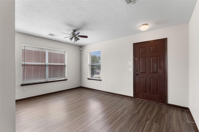 empty room with a textured ceiling, a ceiling fan, dark wood-style flooring, and baseboards