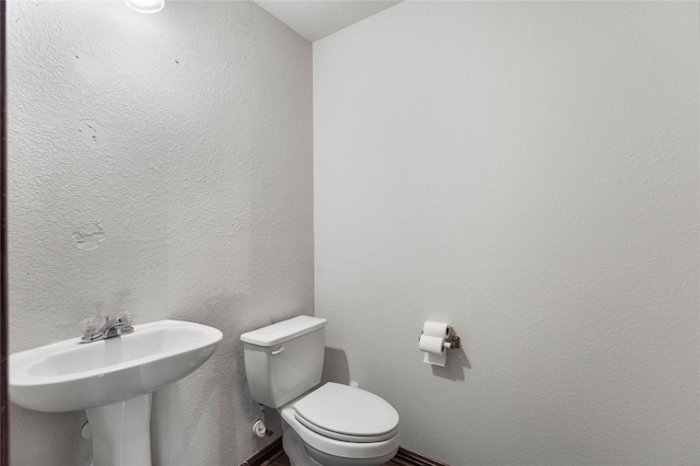 half bathroom with toilet, a textured wall, and a sink