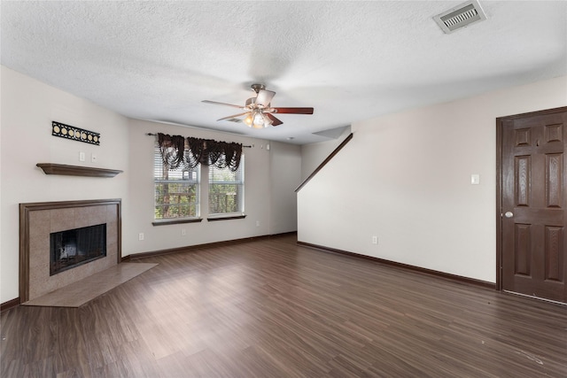 unfurnished living room featuring a tiled fireplace, visible vents, dark wood-type flooring, and ceiling fan