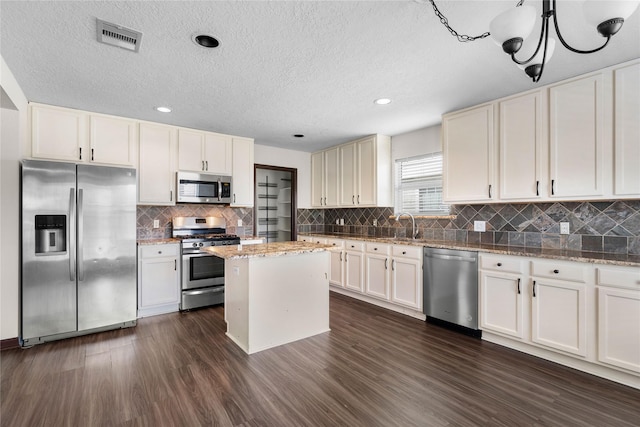 kitchen with visible vents, backsplash, a kitchen island, stainless steel appliances, and dark wood-style flooring