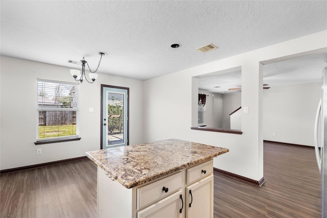 kitchen with dark wood finished floors, light stone countertops, visible vents, and baseboards