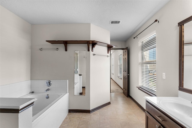 full bath with visible vents, a textured ceiling, baseboards, a bath, and vanity