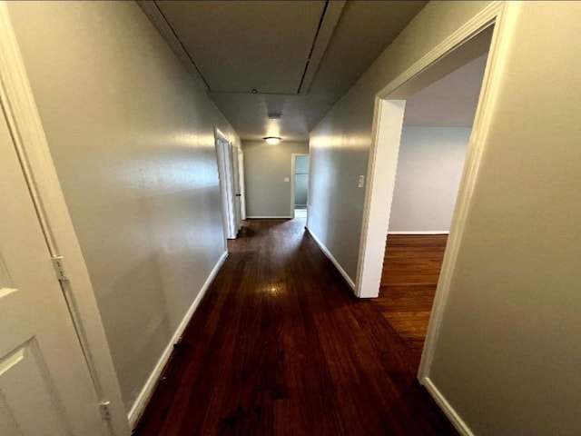 corridor featuring attic access, baseboards, and wood finished floors