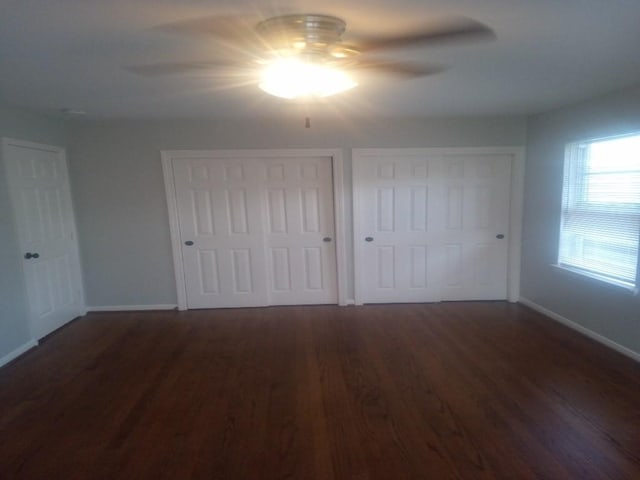 unfurnished bedroom with a ceiling fan, wood finished floors, multiple closets, and baseboards