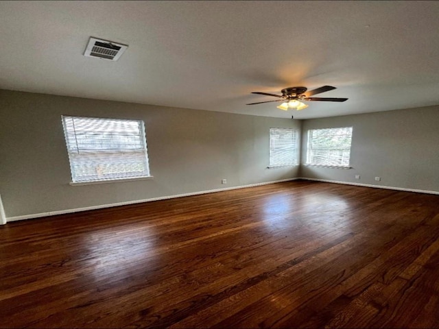 empty room featuring ceiling fan, visible vents, baseboards, and dark wood finished floors