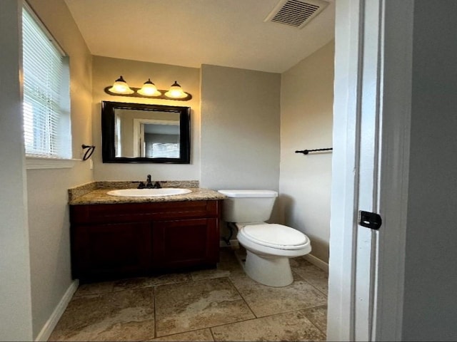 half bath featuring visible vents, baseboards, toilet, and vanity