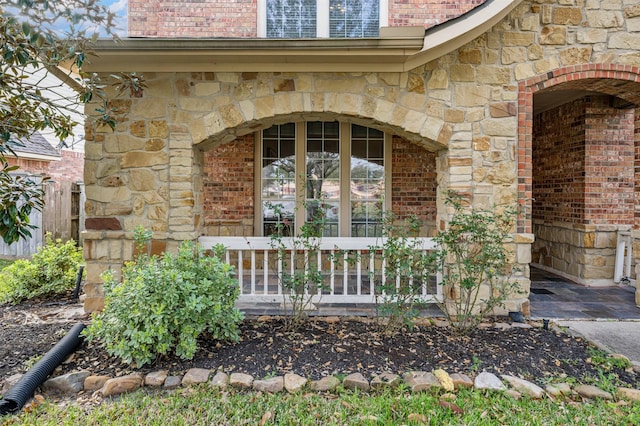 property entrance with fence, brick siding, stone siding, and covered porch