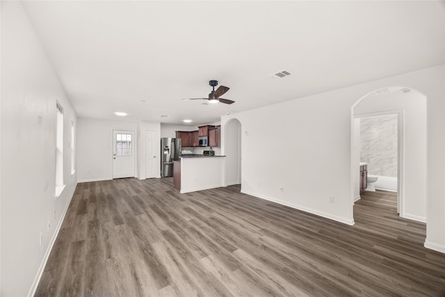 unfurnished living room featuring dark wood-style floors, visible vents, baseboards, arched walkways, and ceiling fan