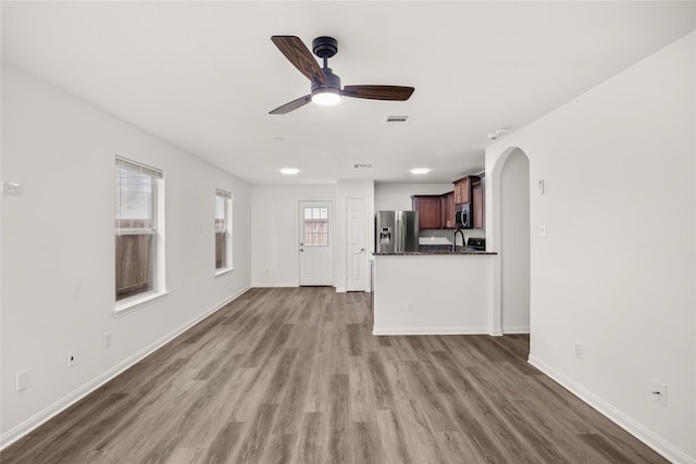 unfurnished living room featuring visible vents, baseboards, ceiling fan, wood finished floors, and arched walkways