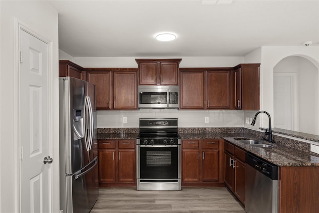 kitchen with dark stone countertops, light wood-style flooring, a sink, stainless steel appliances, and tasteful backsplash