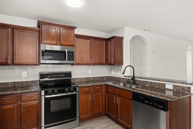 kitchen with dark stone countertops, a peninsula, a sink, decorative backsplash, and stainless steel appliances