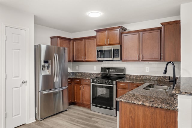 kitchen featuring dark stone countertops, light wood finished floors, a sink, appliances with stainless steel finishes, and brown cabinets