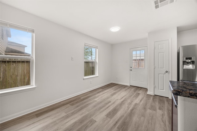 unfurnished dining area featuring light wood-style flooring, a healthy amount of sunlight, visible vents, and baseboards