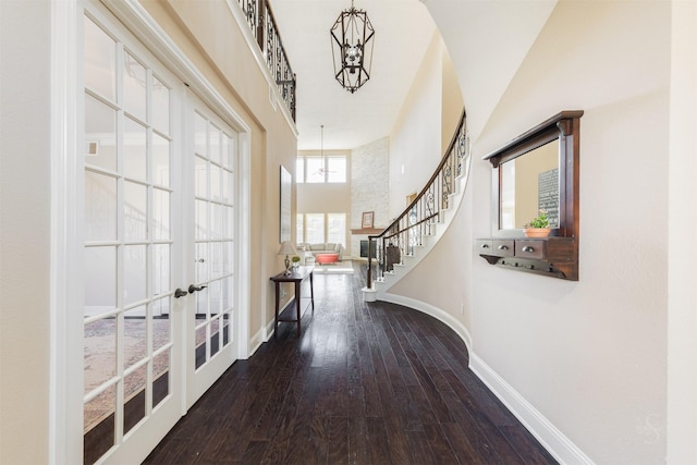 corridor with wood finished floors, baseboards, a high ceiling, stairs, and french doors