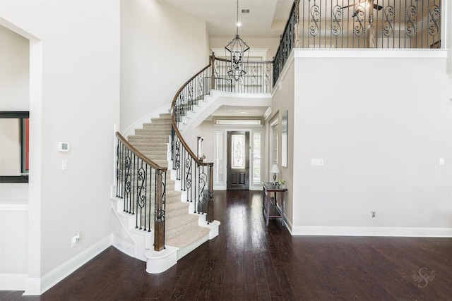 foyer entrance featuring baseboards, stairs, hardwood / wood-style flooring, a towering ceiling, and a notable chandelier