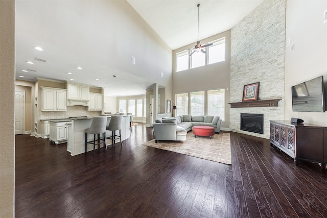 living area featuring recessed lighting, visible vents, a stone fireplace, and dark wood-style flooring