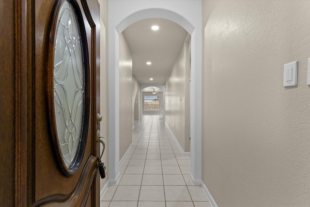 hallway featuring arched walkways, light tile patterned floors, and baseboards