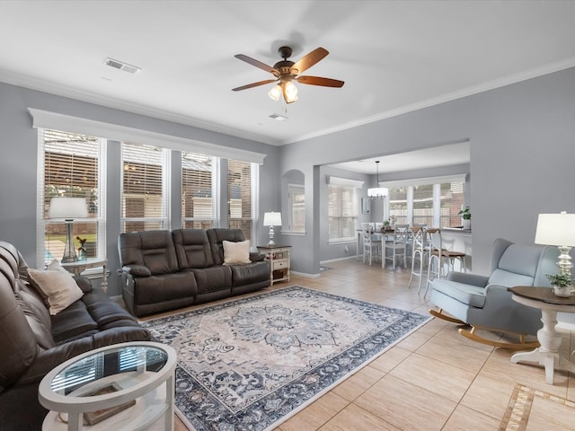 living area with tile patterned flooring, visible vents, baseboards, ceiling fan, and ornamental molding