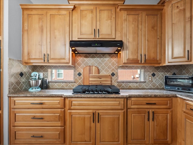 kitchen with under cabinet range hood, a toaster, tasteful backsplash, and black cooktop