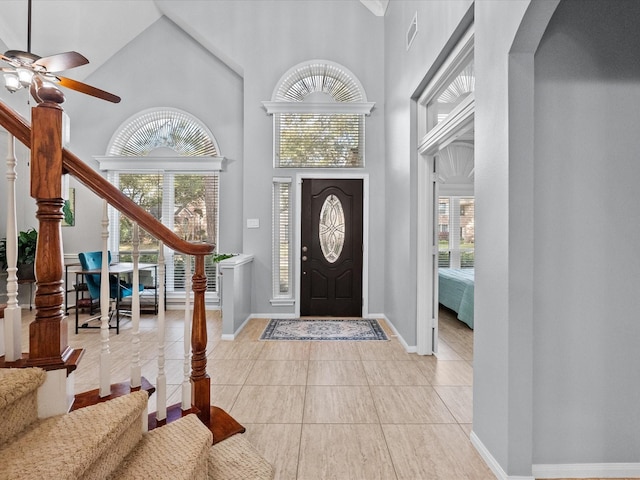 foyer featuring visible vents, baseboards, stairway, a towering ceiling, and a ceiling fan