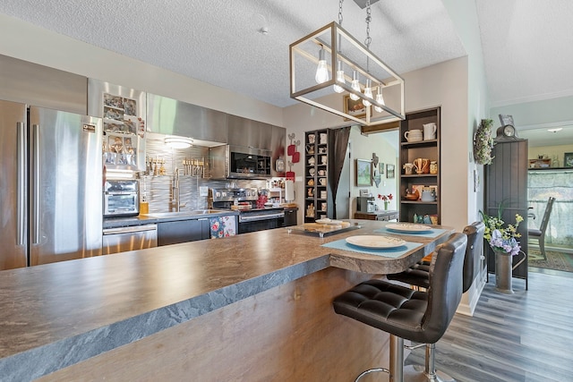 interior space with wood finished floors, appliances with stainless steel finishes, dark countertops, a kitchen bar, and a sink