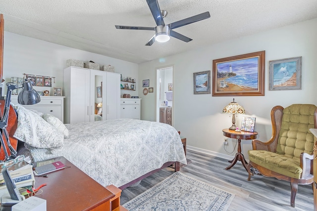 bedroom with ensuite bath, a ceiling fan, baseboards, a textured ceiling, and wood finished floors