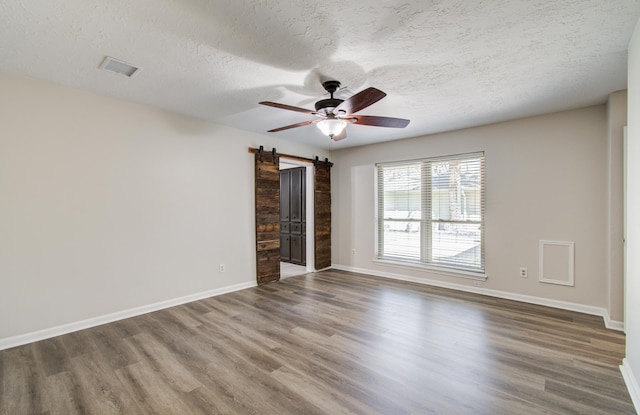 spare room featuring a ceiling fan, a textured ceiling, wood finished floors, a barn door, and baseboards