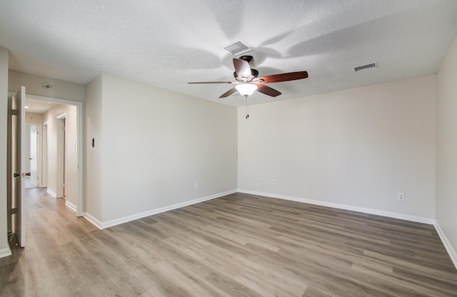 spare room featuring visible vents, baseboards, ceiling fan, wood finished floors, and a textured ceiling