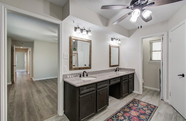 bathroom featuring wood finished floors, a ceiling fan, double vanity, and a sink