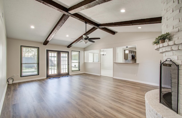 unfurnished living room with ceiling fan with notable chandelier, wood finished floors, a fireplace, baseboards, and vaulted ceiling with beams