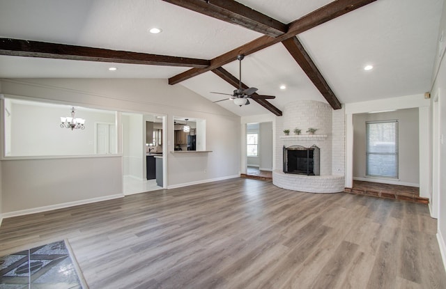 unfurnished living room with a brick fireplace, baseboards, lofted ceiling with beams, ceiling fan with notable chandelier, and wood finished floors