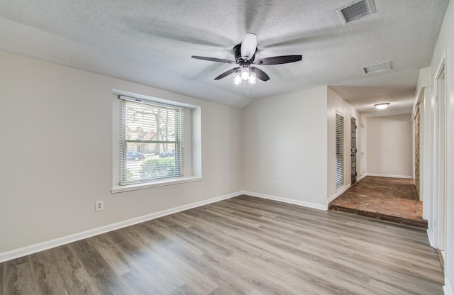 empty room with a textured ceiling, wood finished floors, visible vents, and baseboards