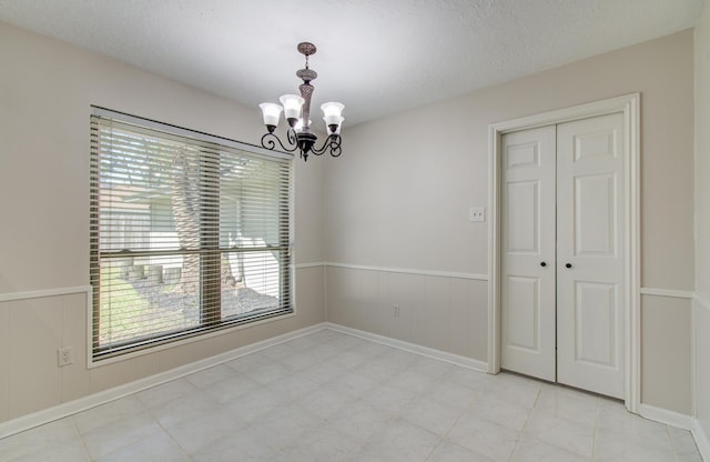 unfurnished dining area with a chandelier, a wainscoted wall, and a textured ceiling