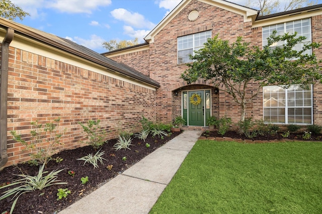 view of exterior entry featuring a lawn and brick siding