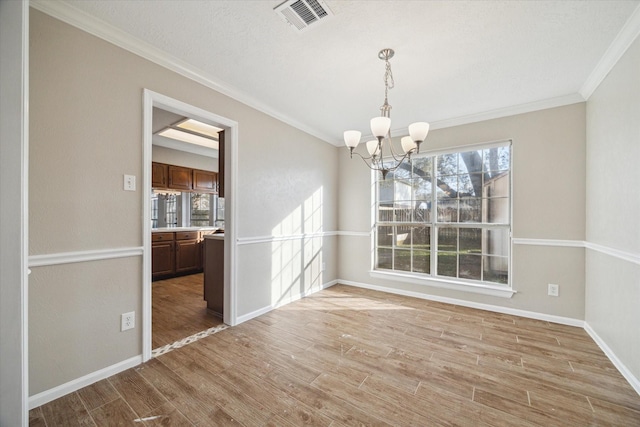 unfurnished dining area with baseboards, visible vents, light wood-style flooring, crown molding, and a notable chandelier